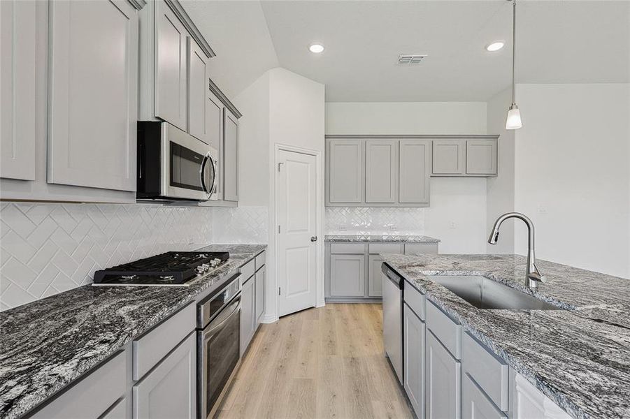 Kitchen with light hardwood / wood-style flooring, tasteful backsplash, hanging light fixtures, stainless steel appliances, and gray cabinets