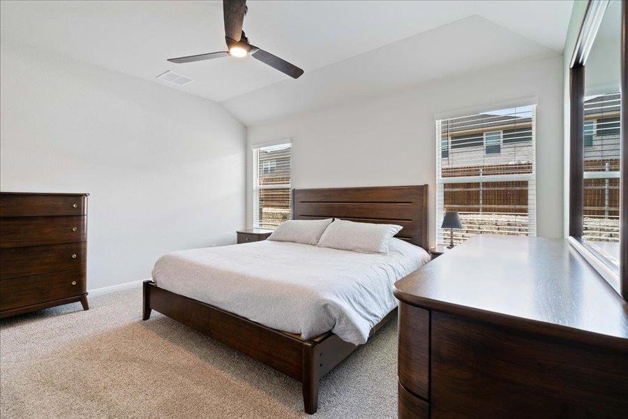 Carpeted bedroom featuring a ceiling fan, baseboards, lofted ceiling, and visible vents