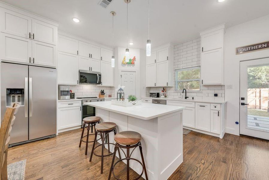 Kitchen with stainless steel appliances, a kitchen bar, a kitchen island, white cabinetry, and dark wood finished floors