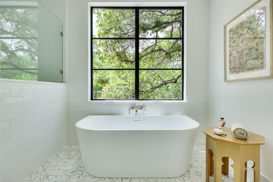 Freestanding soaking tub centered beneath a large window with black grid framing