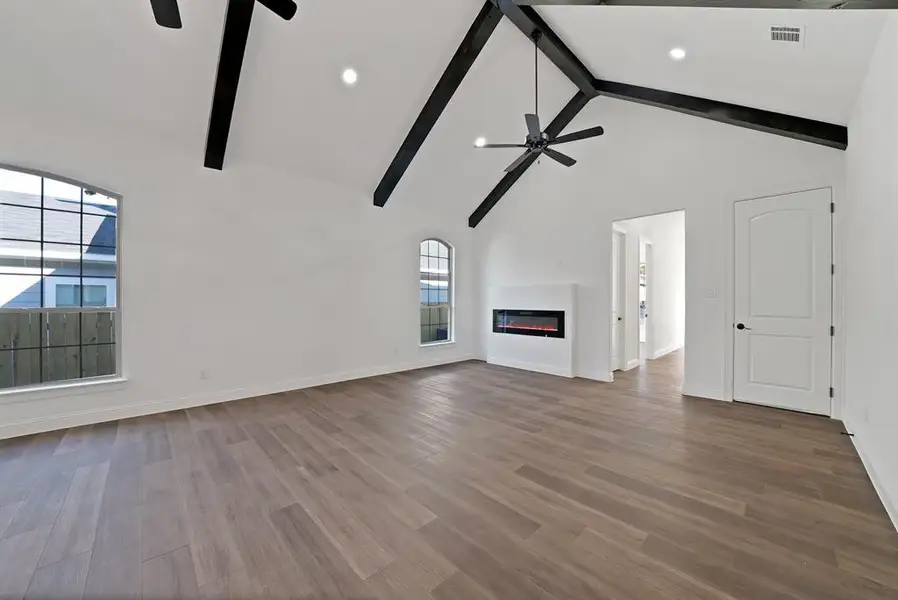 Unfurnished living room featuring dark wood-style flooring, a glass covered fireplace, high vaulted ceiling, ceiling fan, and beamed ceiling