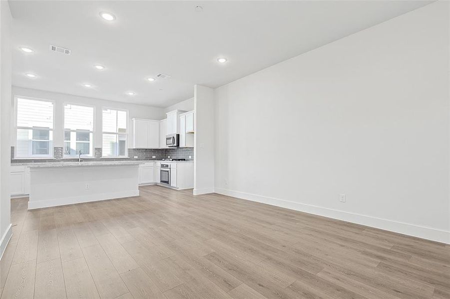 Open concept living area with light-toned flooring, recessed lighting, and a modern kitchen featuring a white island and white cabinetry