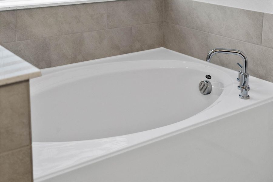 Indulge in the primary bath's deep, built-in soaking tub with elegant chrome fixtures and a sleek tile surround for a true spa-like retreat.