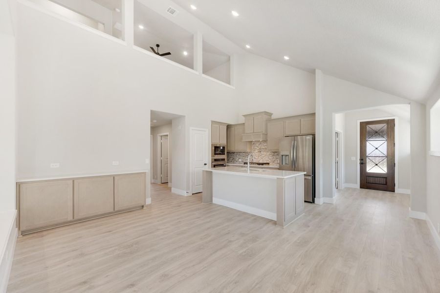 Open-concept kitchen with large island, gray cabinets, stainless appliances, and high vaulted ceilings over light wood floors