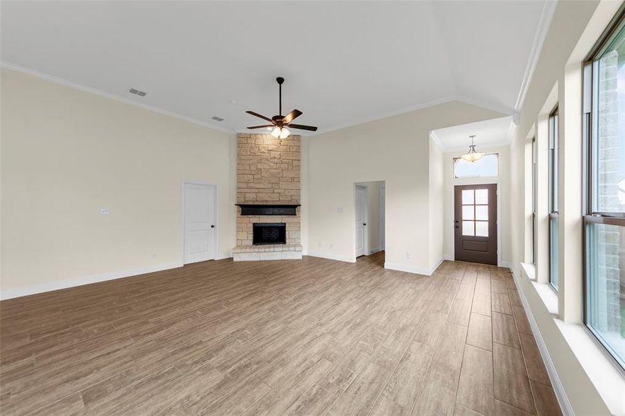 Spacious living area featuring vaulted ceilings, wood-look tile flooring, a stone fireplace, and abundant natural light from multiple windows