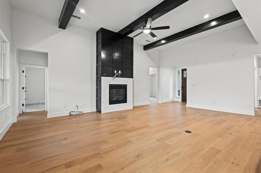 Unfurnished living room featuring beamed ceiling, light wood finished floors, a premium fireplace, a ceiling fan, and a towering ceiling