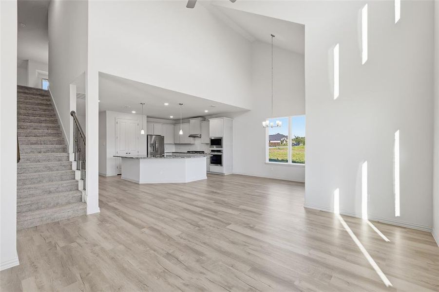 Unfurnished living room featuring light wood finished floors, a high ceiling, suspended lighting, and ceiling fan Unfurnished living room featuring light wood finished floors, a high ceiling, suspended lighting, and ceiling fan