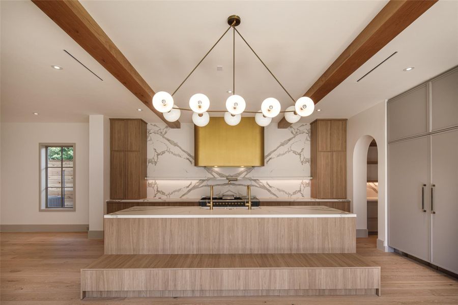 Warm wood cabinetry, dramatic veined stone, exposed beams, and that showstopping brass hood create a room that feels custom from every angle. The oversized island, and its built-in seating, was made for the way people actually gather.