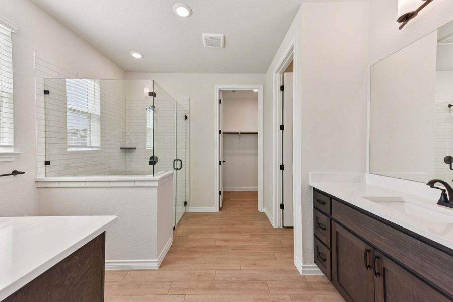 Bathroom featuring two vanities, a shower stall, light wood-style floors, a walk in closet, and recessed lighting