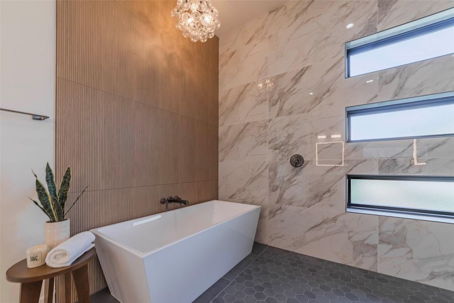 Bathroom featuring a freestanding bath, tile walls, a chandelier, and dark tile patterned flooring