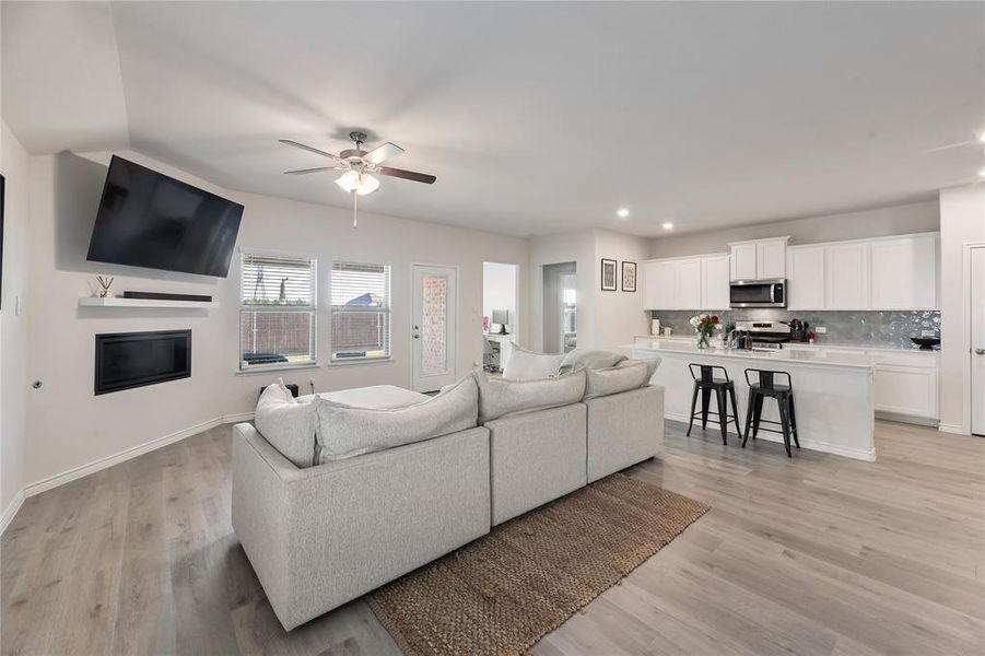 Living room with light wood finished floors, a glass covered fireplace, ceiling fan, and recessed lighting