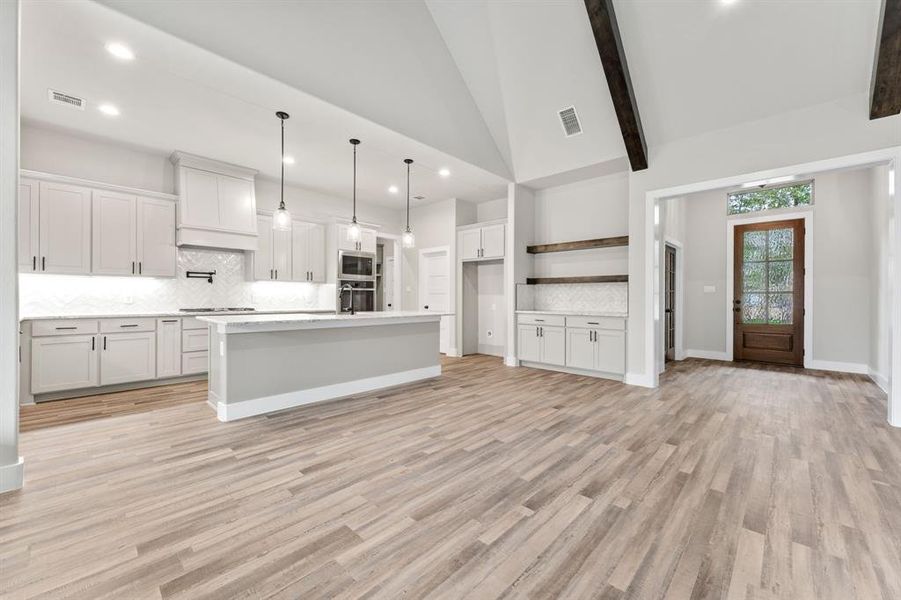 Kitchen with white cabinetry, decorative backsplash, a center island with sink, and decorative light fixtures