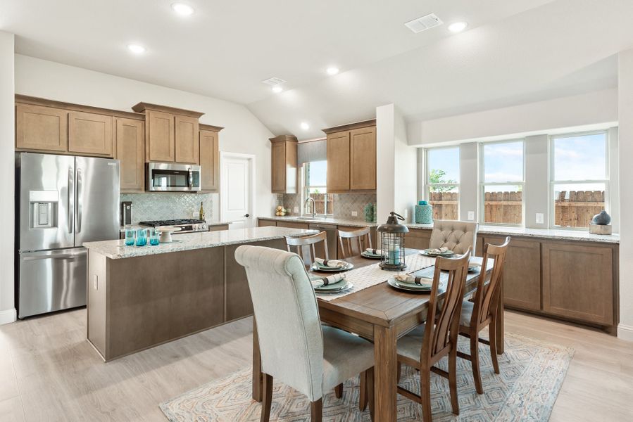Open kitchen and dining area with wood cabinets, granite island, stainless appliances, and a six-seat dining table near large windows Open kitchen and dining area with wood cabinets, granite island, stainless appliances, and a six-seat dining table near large windows