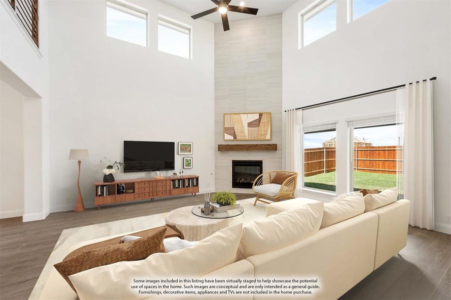 Living room with two-story ceiling, fireplace, ceiling fan, and large windows overlooking backyard