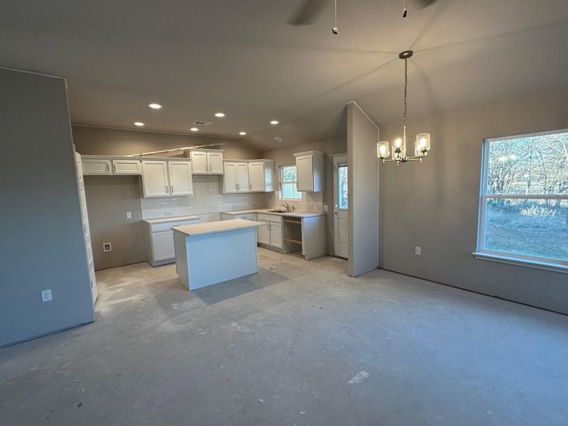 Kitchen featuring white cabinetry, tasteful backsplash, a notable chandelier, lofted ceiling, and a center island