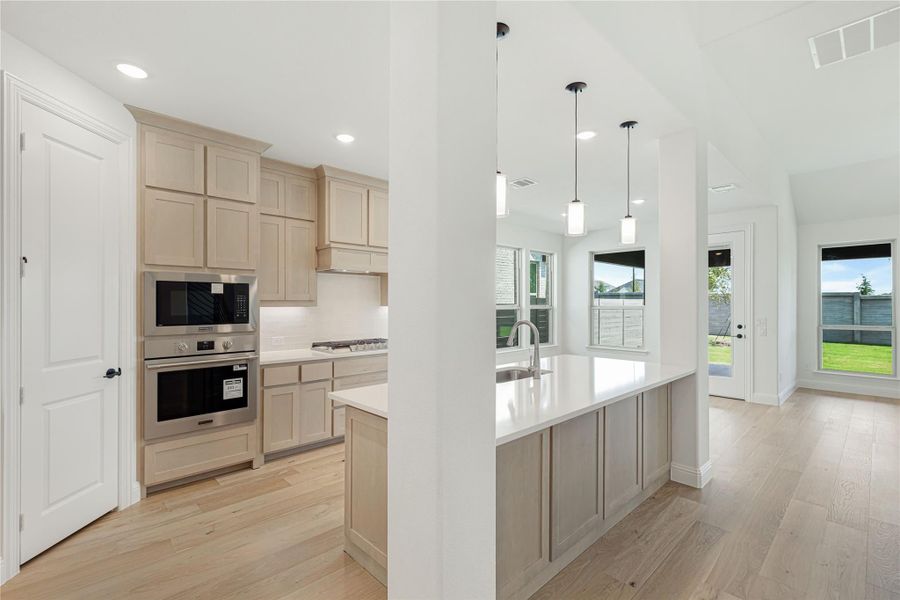 Kitchen with light wood cabinets, stainless steel appliances, center island, and pendant lights over white countertops Kitchen with light wood cabinets, stainless steel appliances, center island, and pendant lights over white countertops