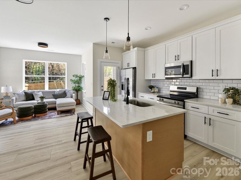 Bright, open-concept kitchen featuring a spacious island with seating, stainless steel appliances, and seamless flow into the sun-filled living area.