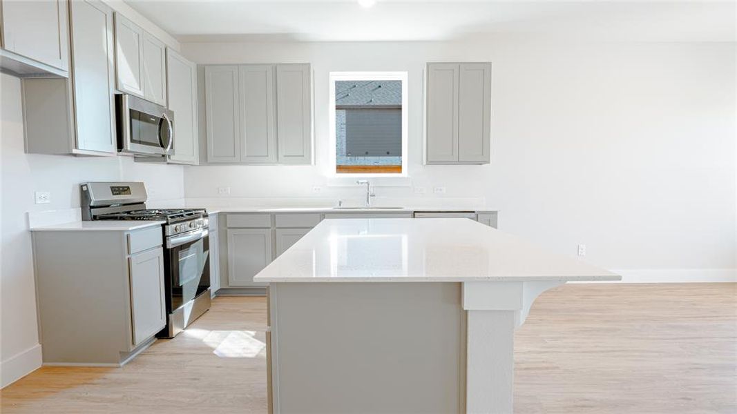 Kitchen featuring appliances with stainless steel finishes, light wood-type flooring, sink, gray cabinets, and a kitchen island