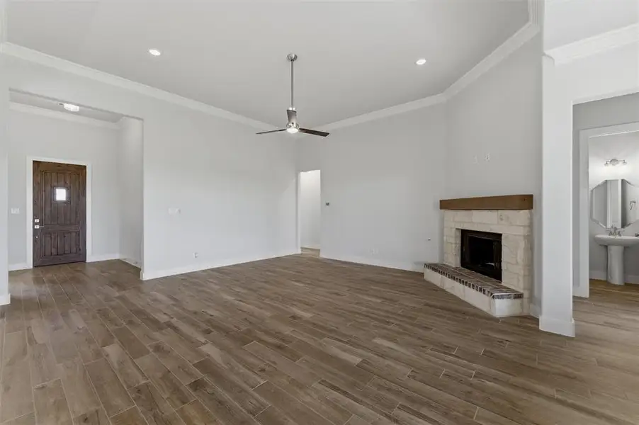 Spacious living area featuring wood-finish flooring, a corner fireplace with a stone surround and wood mantel, crown molding, and a ceiling fan