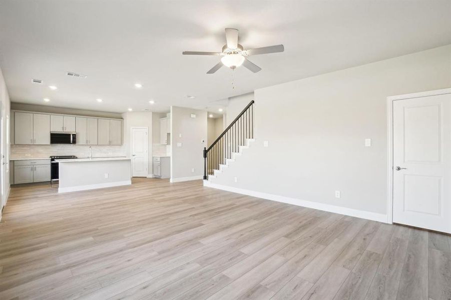Unfurnished living room featuring light wood finished floors, recessed lighting, ceiling fan, and stairway Unfurnished living room featuring light wood finished floors, recessed lighting, ceiling fan, and stairway