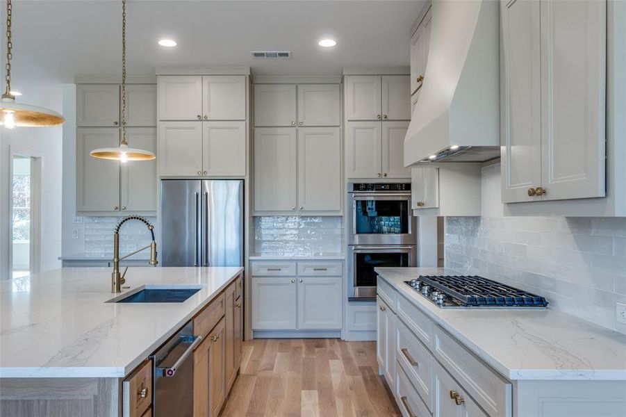 Kitchen with pendant lighting, sink, premium range hood, white cabinetry, and stainless steel appliances