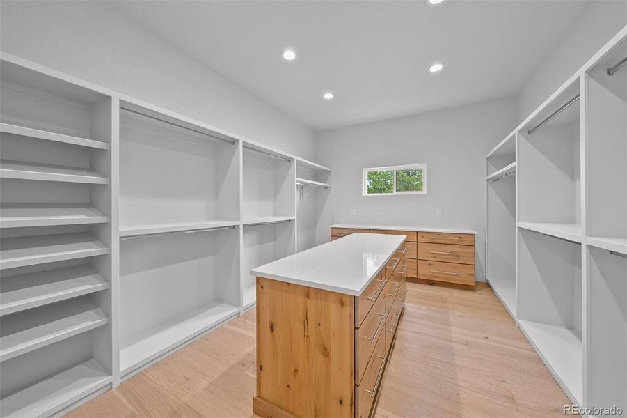 Primary walk-in closet with custom shelving and large island featuring natural stone countertops.