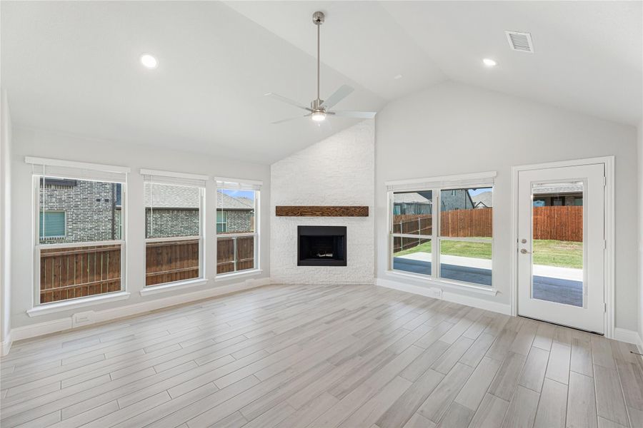 Open living room with vaulted ceiling, brick fireplace, ceiling fan, and light wood floors