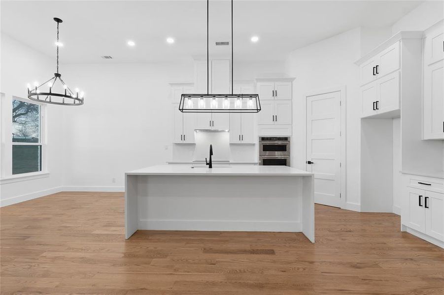 Kitchen featuring white cabinetry, an island with sink, light wood-type flooring, light stone counters, and a breakfast bar
