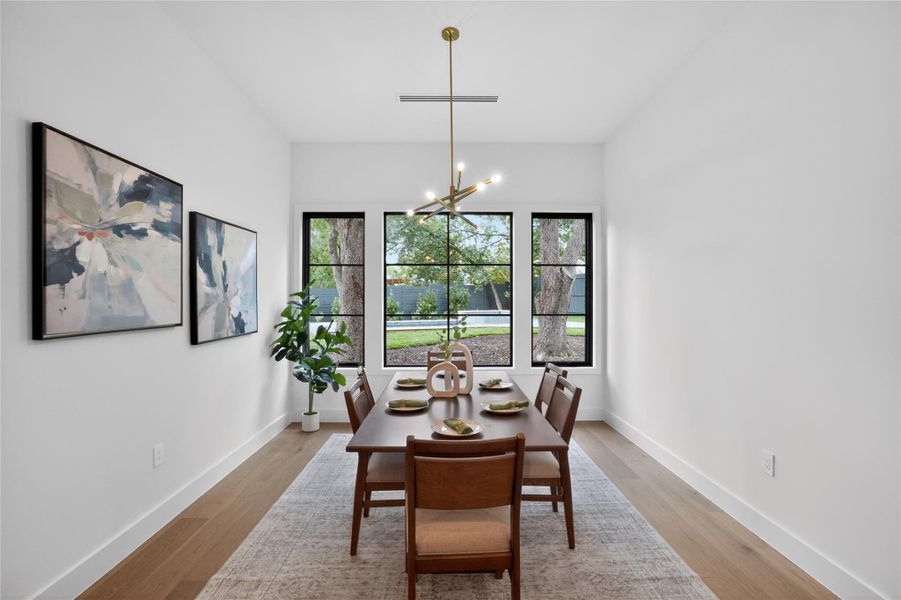 A chic dining space offers views of the lush outdoors through large windows.