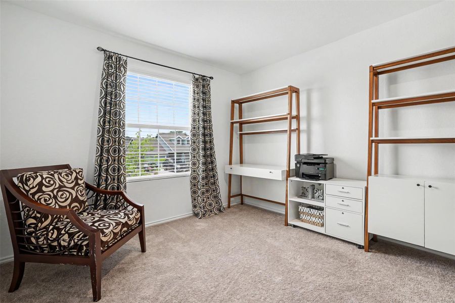 Carpeted room featuring a large window with blinds, white walls, and built-in shelving units with a desk component