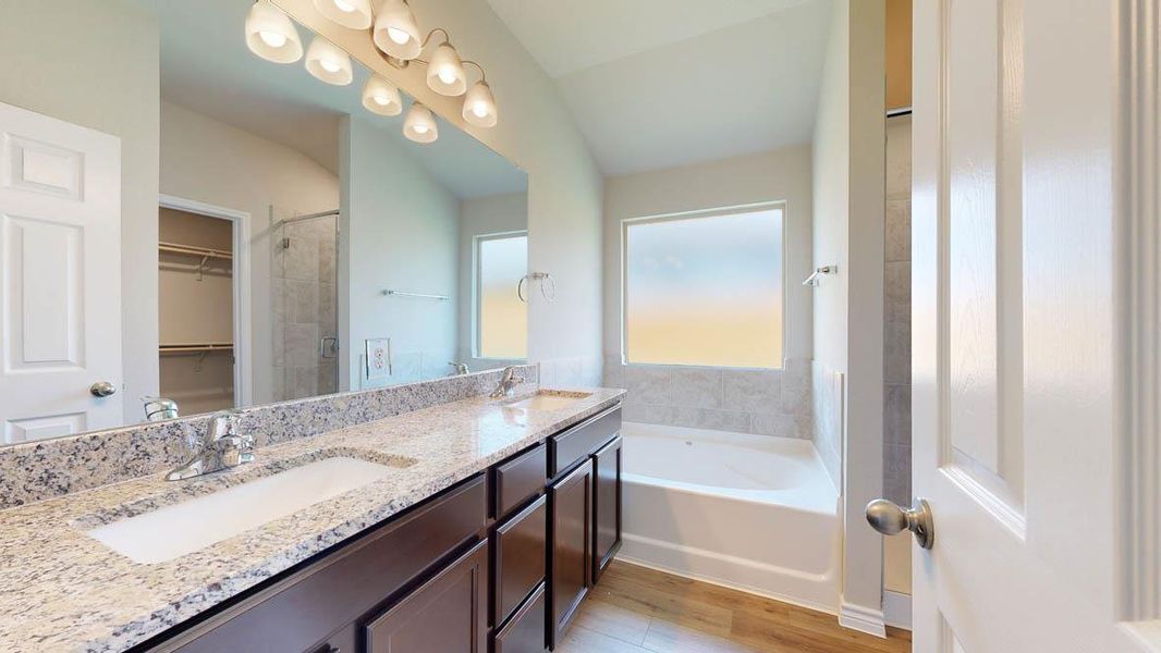 Full bathroom featuring double vanity, a walk in closet, a garden tub, light wood-style flooring, and tiled shower