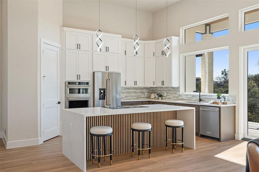 Kitchen with appliances with stainless steel finishes, a breakfast bar, backsplash, a high ceiling, and light stone counters Kitchen with appliances with stainless steel finishes, a breakfast bar, backsplash, a high ceiling, and light stone counters