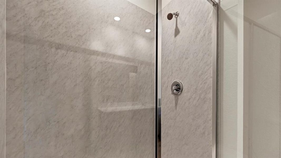 Shower enclosure featuring a chrome shower head and control, glass panel, and light-toned, textured wall finish
