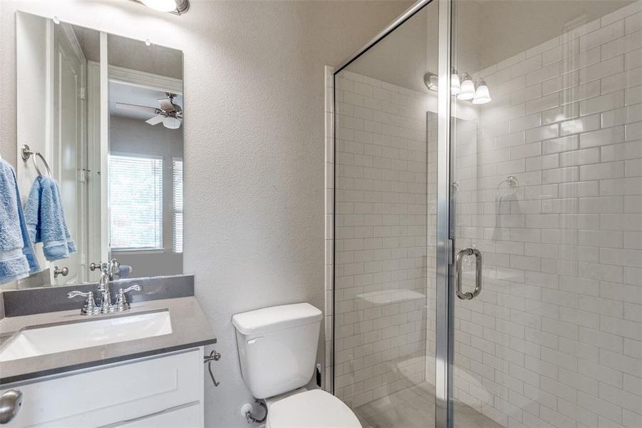 Bathroom featuring ceiling fan, an enclosed shower, toilet, and large vanity