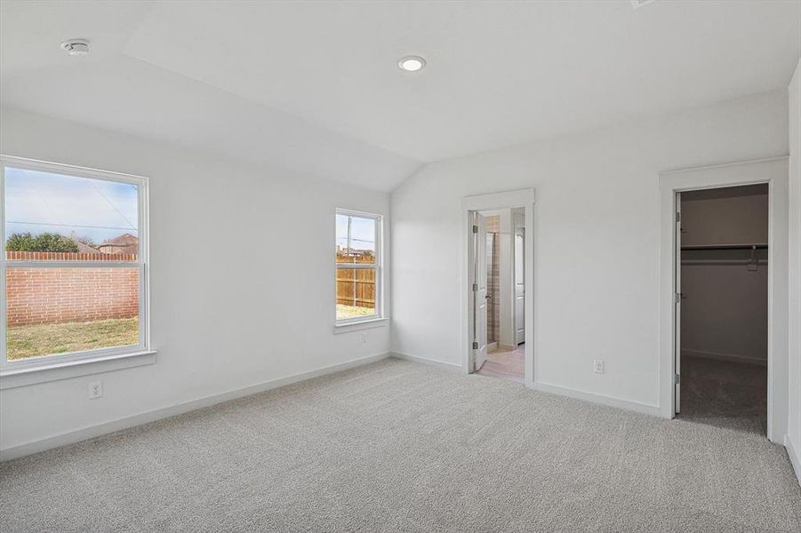 Unfurnished bedroom featuring a closet, a spacious closet, lofted ceiling, ensuite bathroom, and light colored carpet