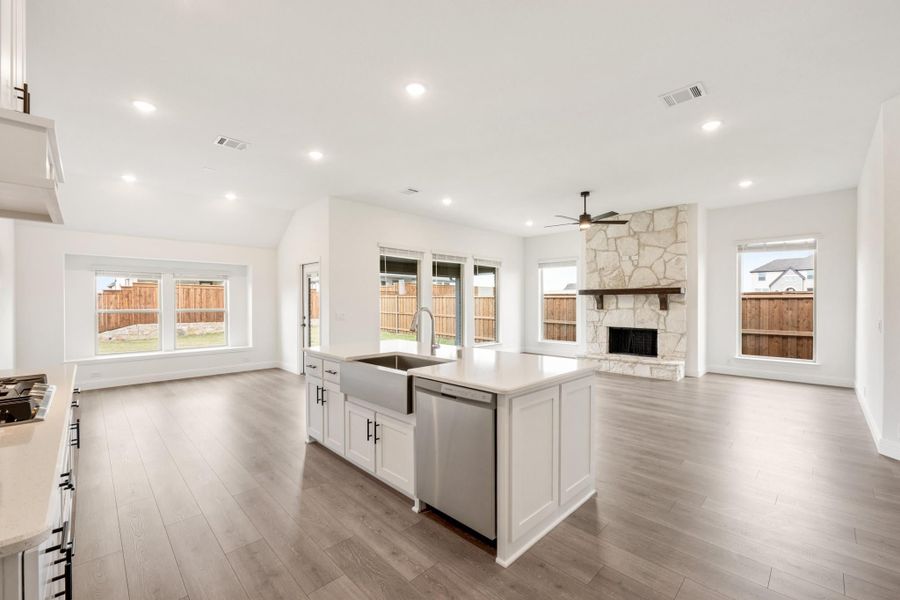 Open-concept kitchen and living area with white island, farmhouse sink, and stone fireplace on hardwood floors