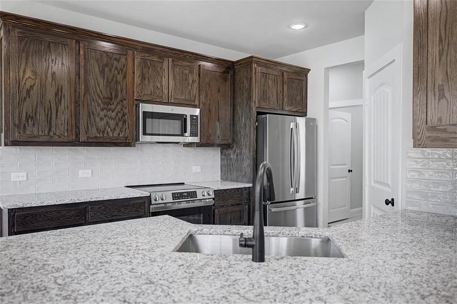 Kitchen featuring dark wood finish cabinetry, stainless steel appliances, light stone counters, and tasteful backsplash
