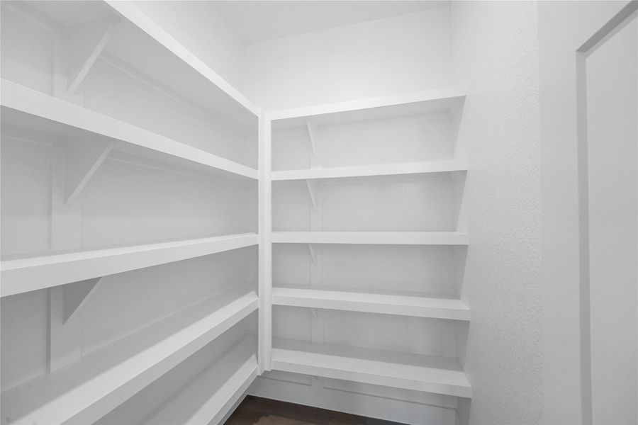 Spacious walk-in pantry offers exceptional storage potential, featuring multiple tiers of sturdy, built-in white shelving. Designed for maximum organization, the deep shelves provide ample space for all your culinary needs.