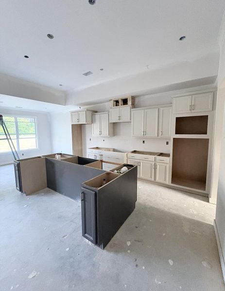 Recessed lighting, tray ceiling, light-toned upper cabinetry, dark-toned island cabinetry, and large windows