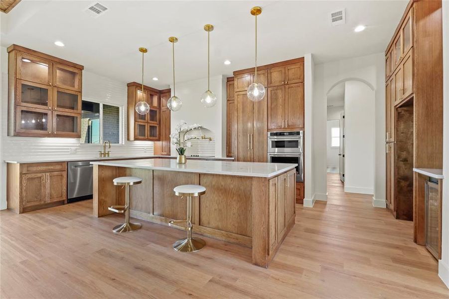 Kitchen featuring glass insert cabinets, brown cabinets, arched walkways, a kitchen bar, and recessed lighting Kitchen featuring glass insert cabinets, brown cabinets, arched walkways, a kitchen bar, and recessed lighting