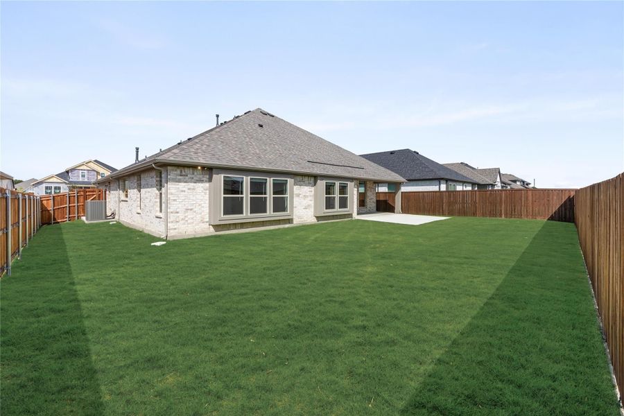Backyard of single-story brick home with large green lawn, concrete patio, and wood privacy fence