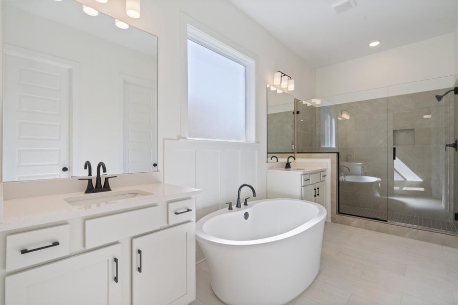 Freestanding soaking tub, dual-sink vanity with light-toned stone countertops, walk-in glass-enclosed shower with tile surround, and matte black fixtures Freestanding soaking tub, dual-sink vanity with light-toned stone countertops, walk-in glass-enclosed shower with tile surround, and matte black fixtures