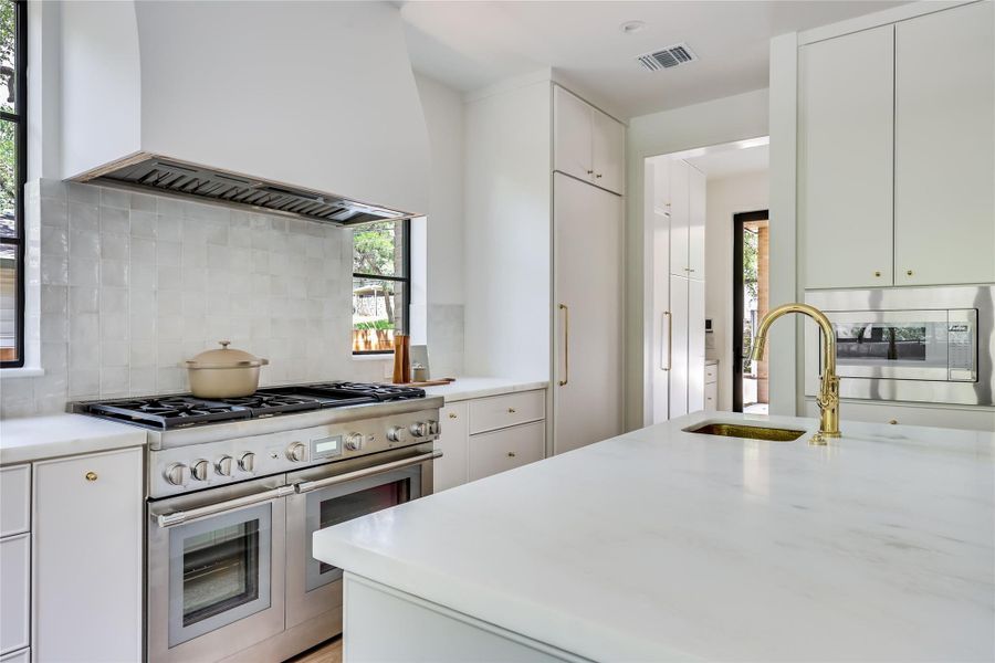 Gourmet kitchen featuring a professional-grade stainless steel range with double ovens, a custom range hood, and a white tile backsplash