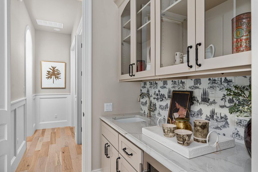 Bar with glass insert cabinets, light stone counters, wainscoting, light wood-type flooring, and a decorative wall