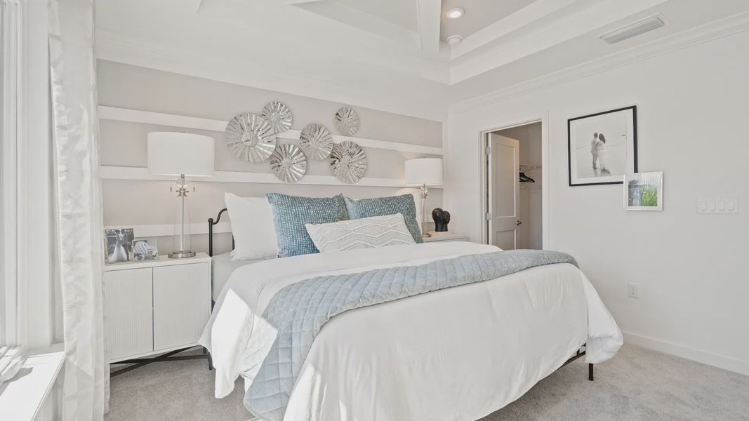 Carpeted primary bedroom with tray ceiling in a DRB Homes Ambersweet model at the Trinity Place community. Carpeted primary bedroom with tray ceiling in a DRB Homes Ambersweet model at the Trinity Place community.