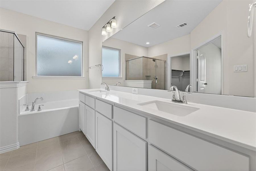Full bathroom featuring double vanity, a shower stall, a spacious closet, light tile patterned floors, and a garden tub