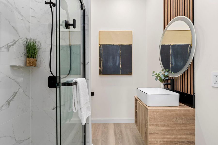 Full bath featuring vanity, a marble finish shower, and light wood finished floors