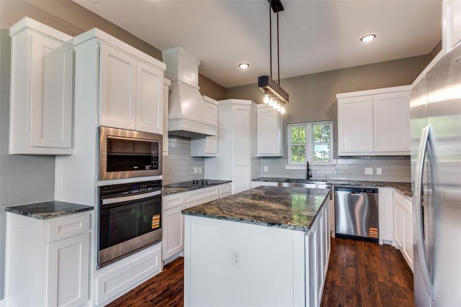 Kitchen with stainless steel appliances, dark stone countertops, decorative backsplash, dark wood-style floors, and a center island Kitchen with stainless steel appliances, dark stone countertops, decorative backsplash, dark wood-style floors, and a center island