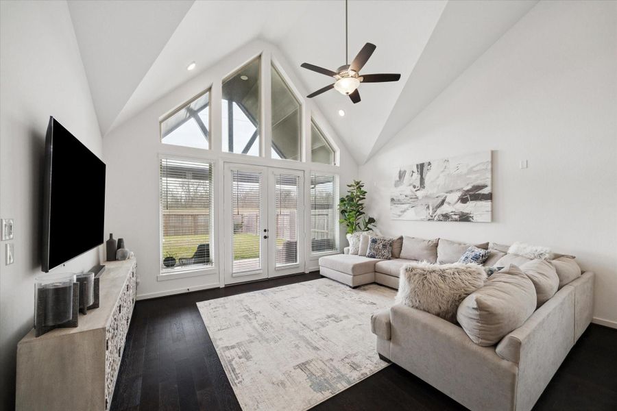 THE FAMILY ROOM FEATURES A TALL VAULTED CEILING WITH A LARGE WALL OF WINDOWS AND GLASS DOORS LEADING TO THE BACKYARD.