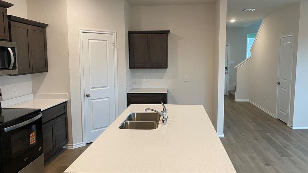 Kitchen with stainless steel appliances, dark wood-type flooring, dark wood finish cabinets, and light stone counters